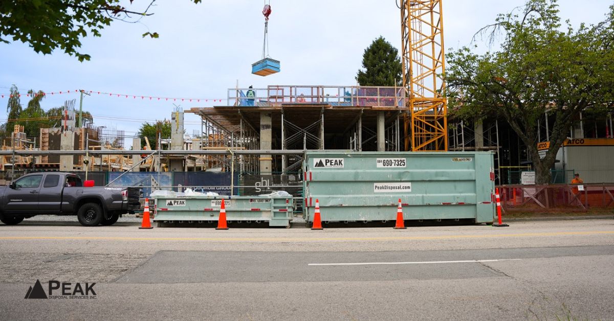 Peak Disposal construction bins positioned beside an active building site with crane, truck, and safety cones.