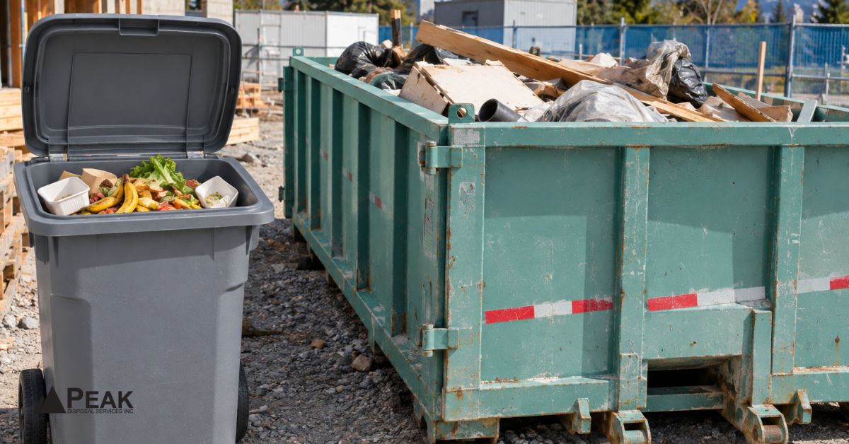 Grey organics bin with food scraps beside green construction dumpster filled with debris on jobsite.