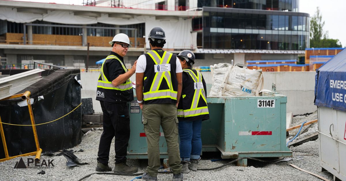 Peak Disposal workers discuss construction waste diversion beside a bin at an active building site.